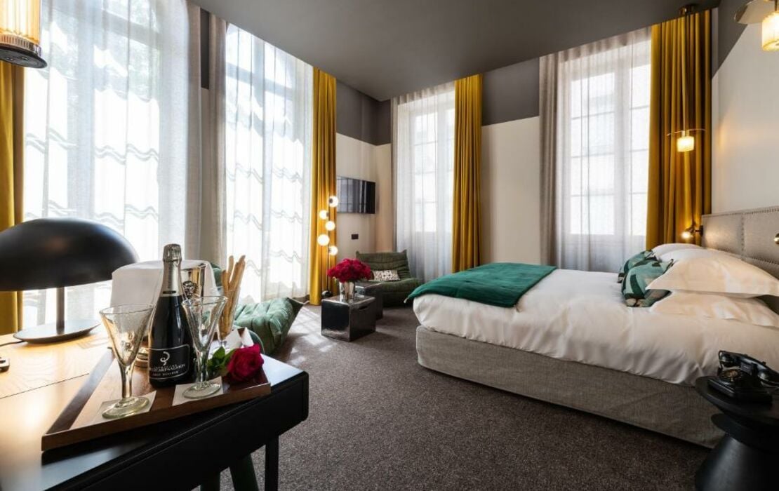 Elegant empty Lyon hotel bedroom with tall windows, modern furniture and warm neutral details